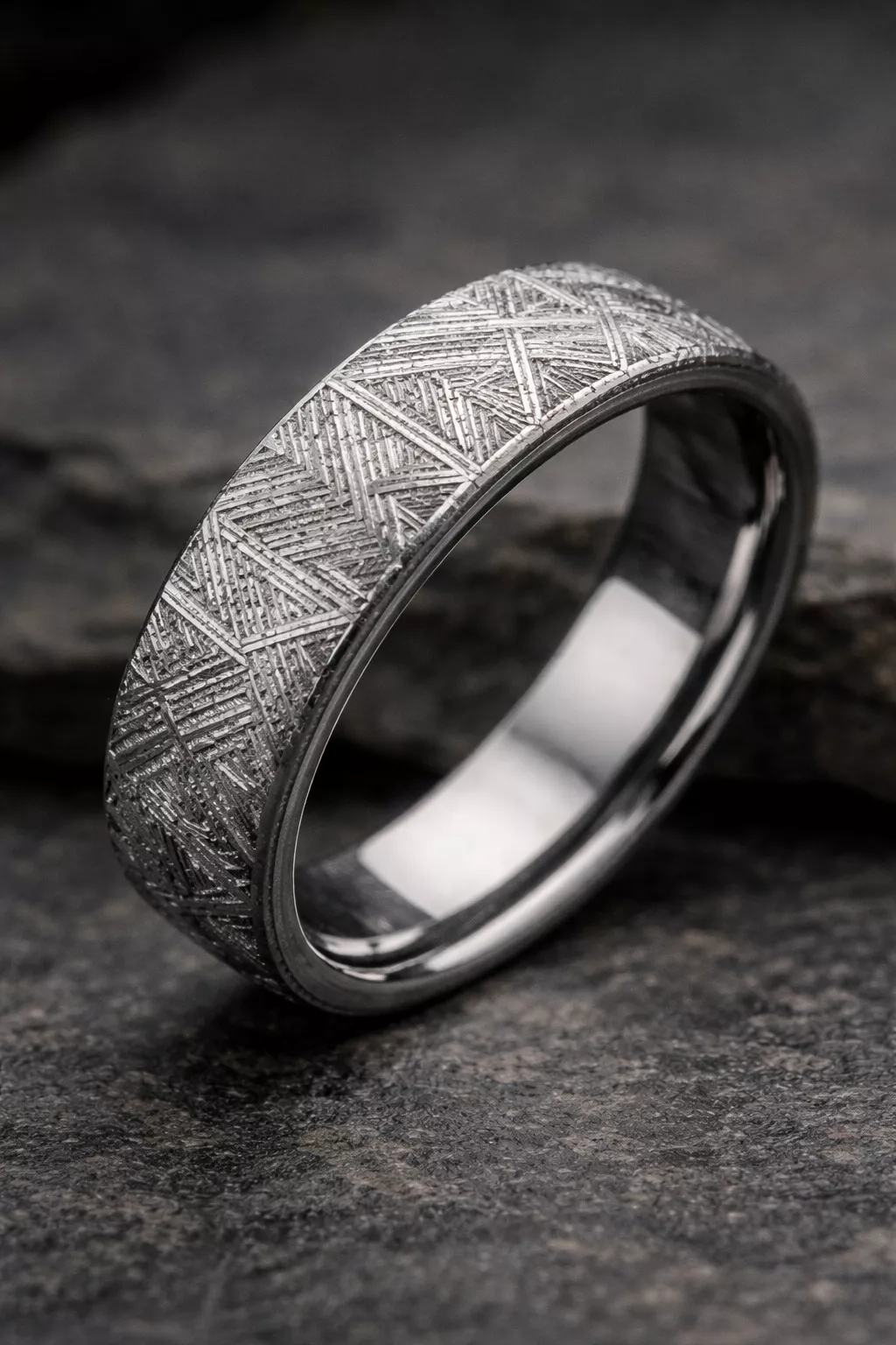 A realistic photo of a wedding band made from grey meteorite showing a distinct geometric Widmanstatten pattern.
