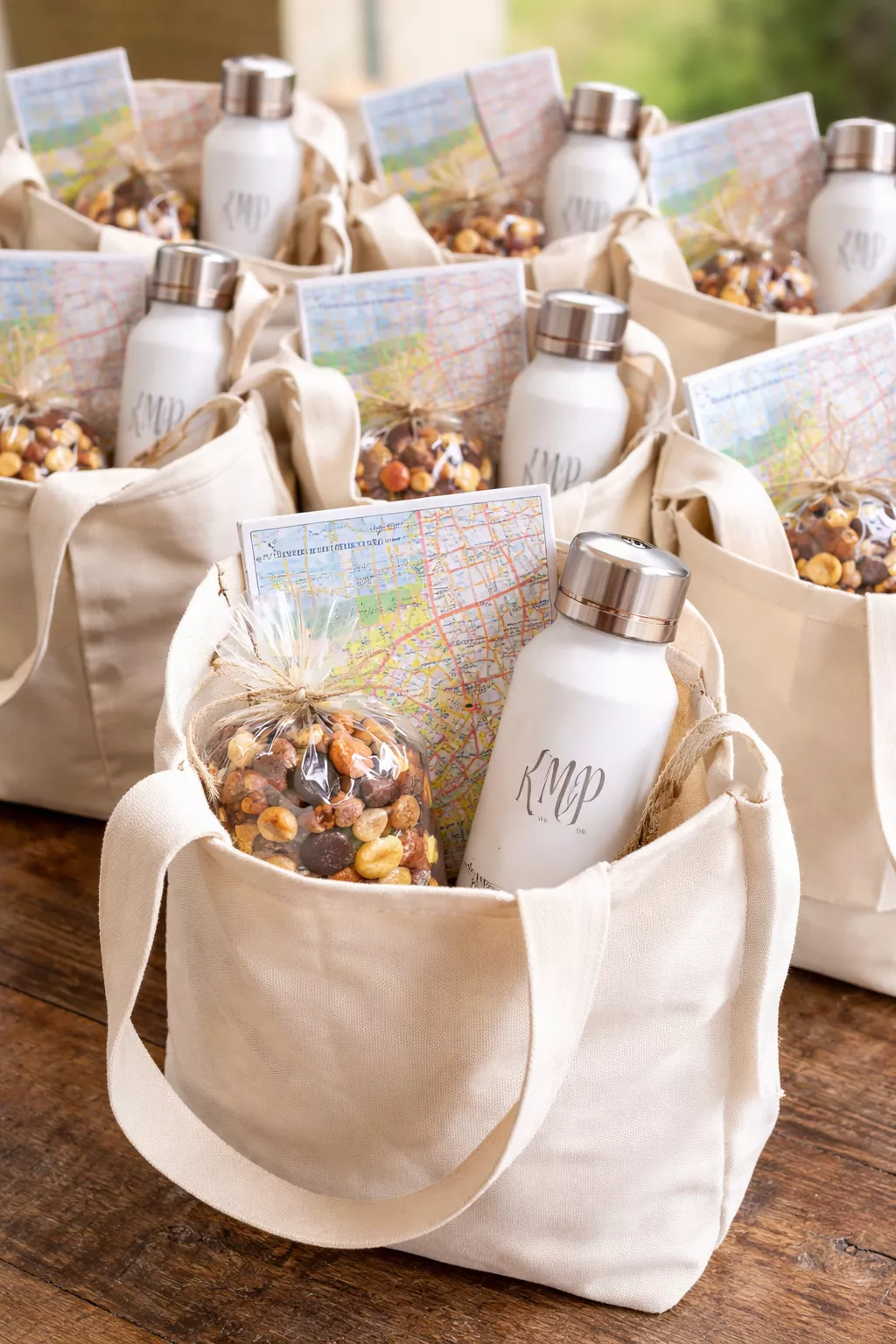 Curated Welcome Experience Bags A realistic photo of several canvas tote bags filled with a local map, a small bag of snacks, and a monogrammed water bottle.