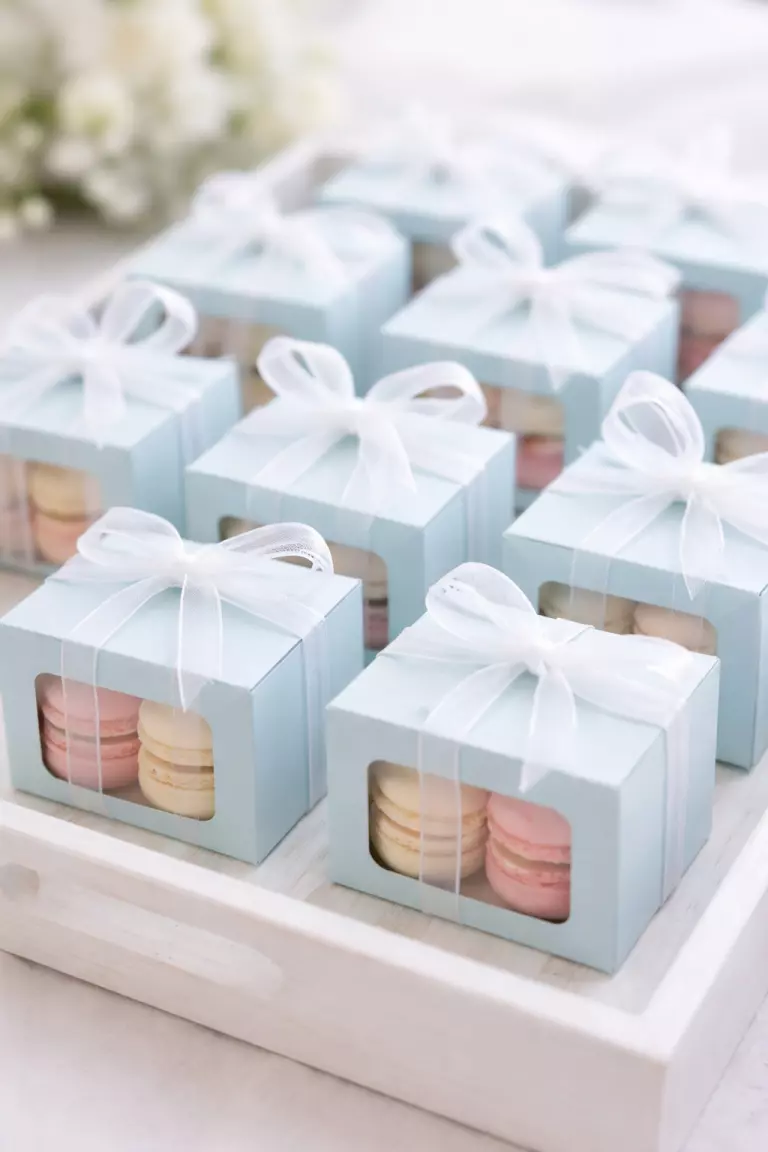 Baby Blue Wedding Favors A realistic photo of small baby blue wedding favor boxes tied with white organza ribbons, containing mini macarons, arranged neatly on a white wooden tray.