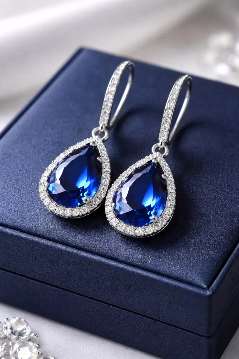 Sapphire Blue Bridesmaid Earrings A realistic photo of a pair of sapphire blue crystal drop earrings in a silver setting, resting on a navy blue jewelry box.