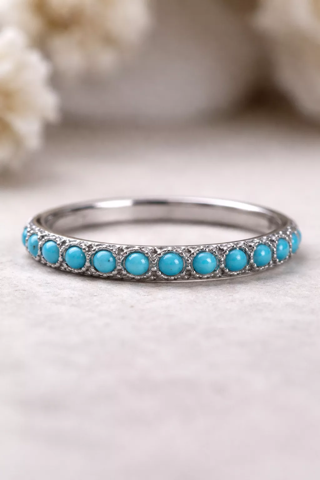 A realistic photo of a stackable silver wedding band with tiny bright blue turquoise cabochons.