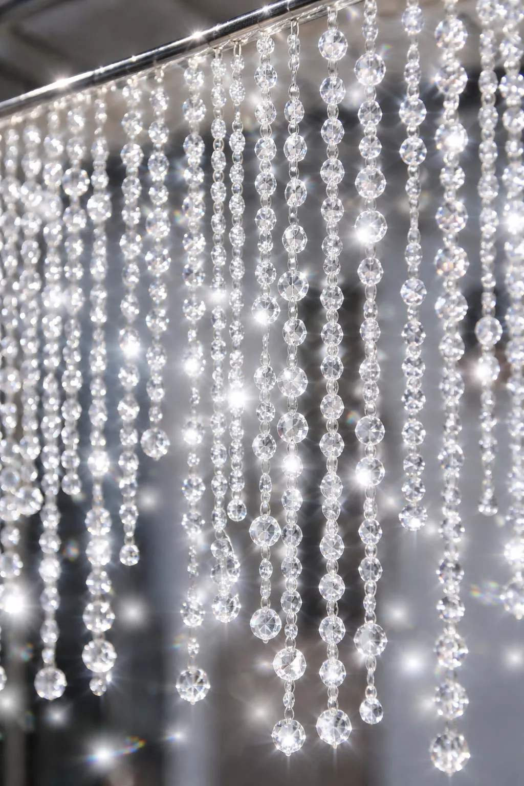 A realistic photo of hundreds of clear crystal beads hanging in strands from a silver rod reflecting sparkly white light.
