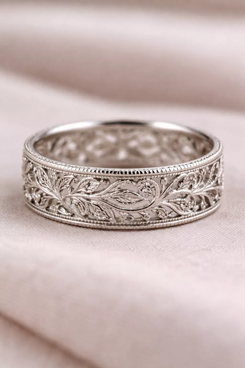 A realistic photo of an intricate silver filigree wedding band with delicate leaf patterns and tiny cutout spaces.