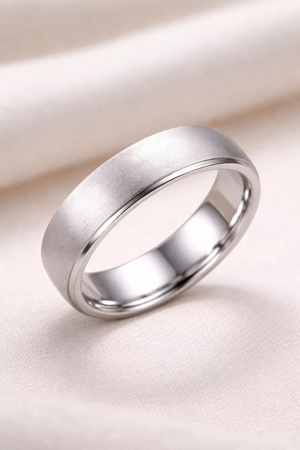 A realistic photo of a satin finish white gold wedding band with a soft velvety texture and polished inner edges.