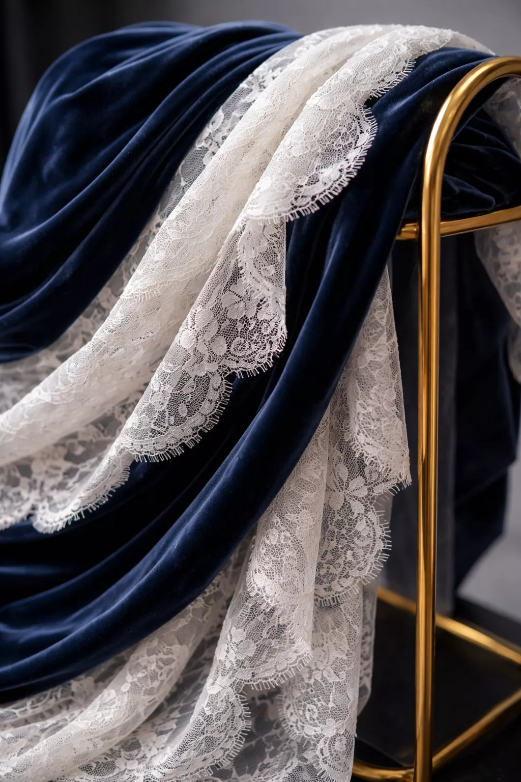 A realistic photo of layers of navy blue velvet and white lace fabric draped over a gold metal frame.