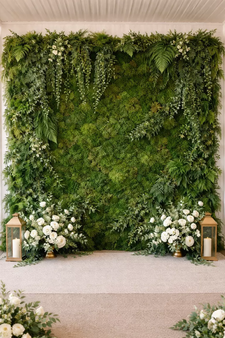 A realistic photo of a lush living wall made of various shades of green moss, ferns, and trailing ivy serving as a backdrop for a wedding photo booth.