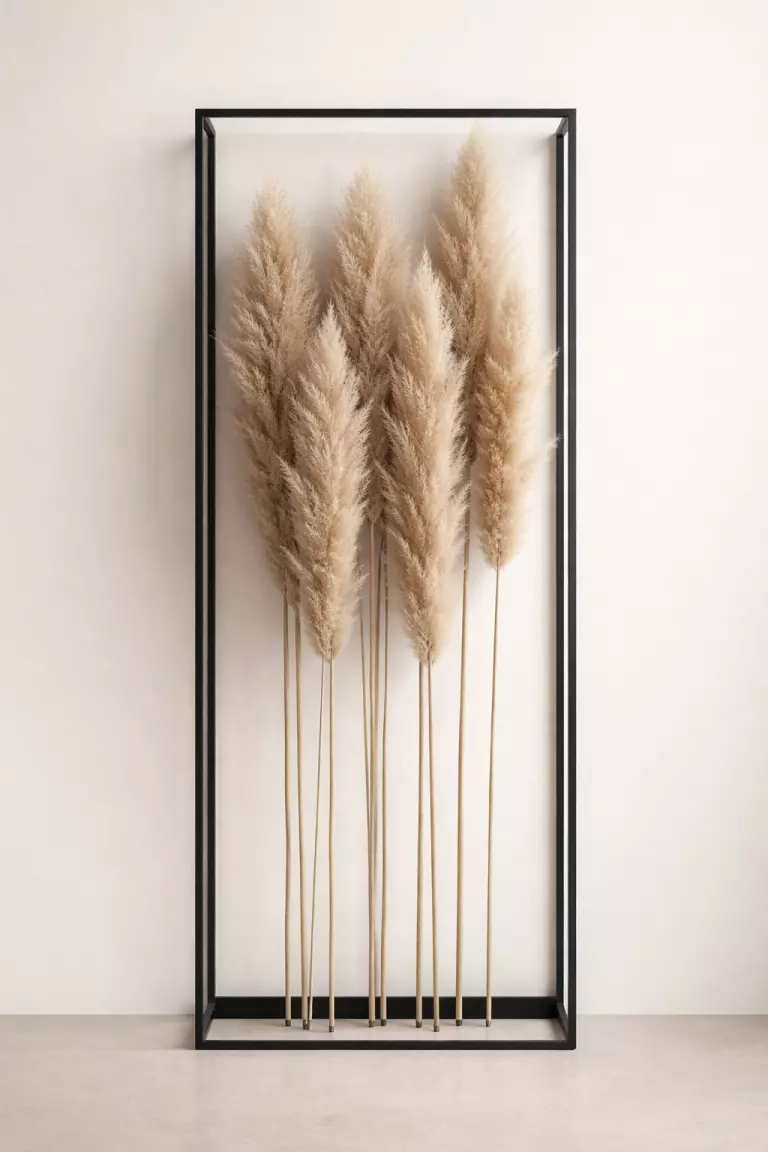 A realistic photo of tall, fluffy pampas grass stems arranged vertically in a minimalist black geometric metal frame against a neutral background.