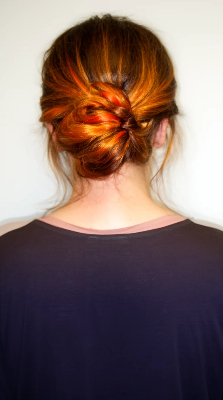 casual photo of a 48-year-old woman wearing a dark top with dark brown hair featuring bright streaks of orange and gold in an updo hairstyle, back view, minimal background