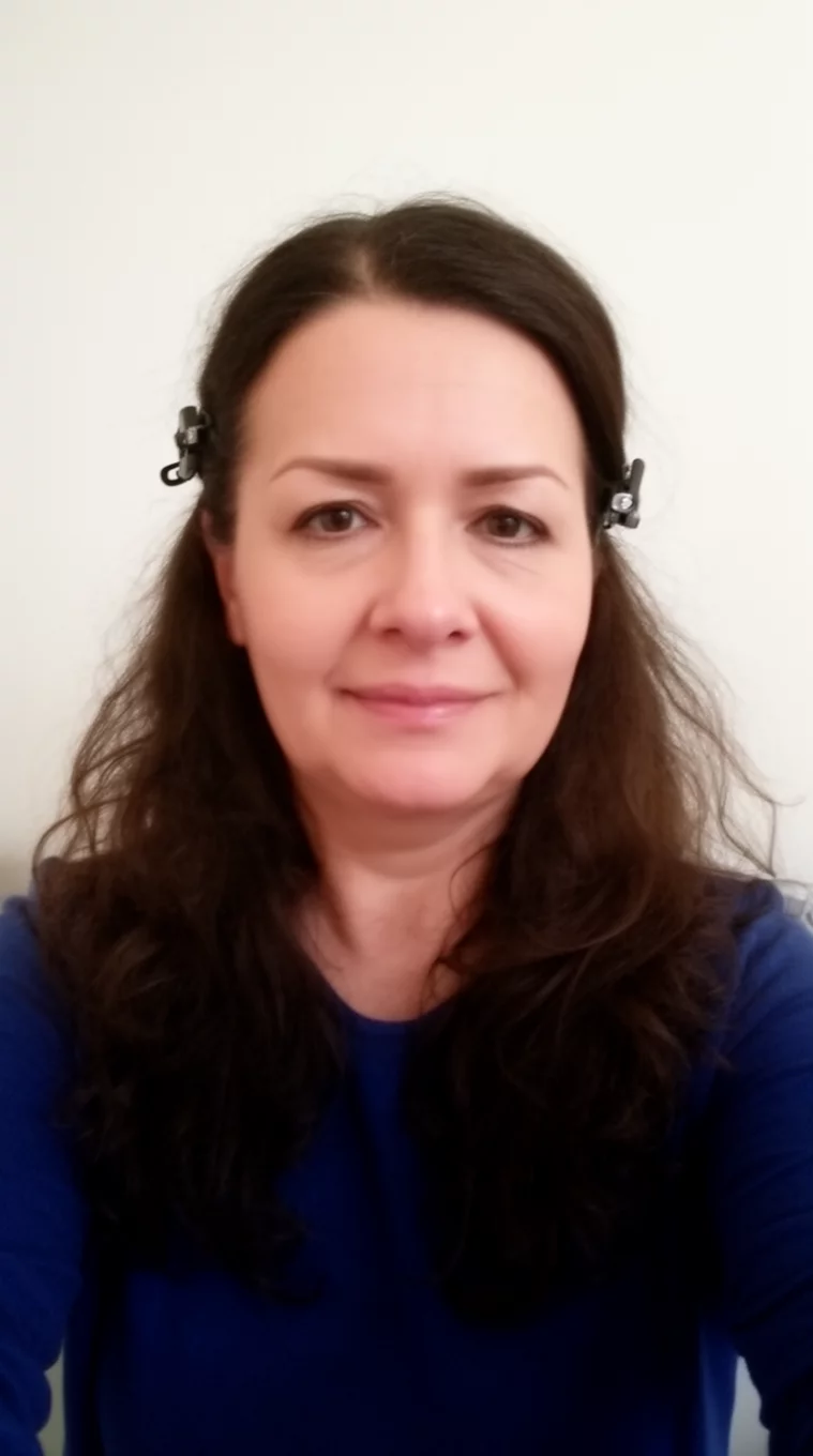 selfie (casual photo if it's a back view shot) of a 45-year-old woman wearing a dark blue top with a long dark brown wavy hair partially clipped back hairstyle, front view, minimal background