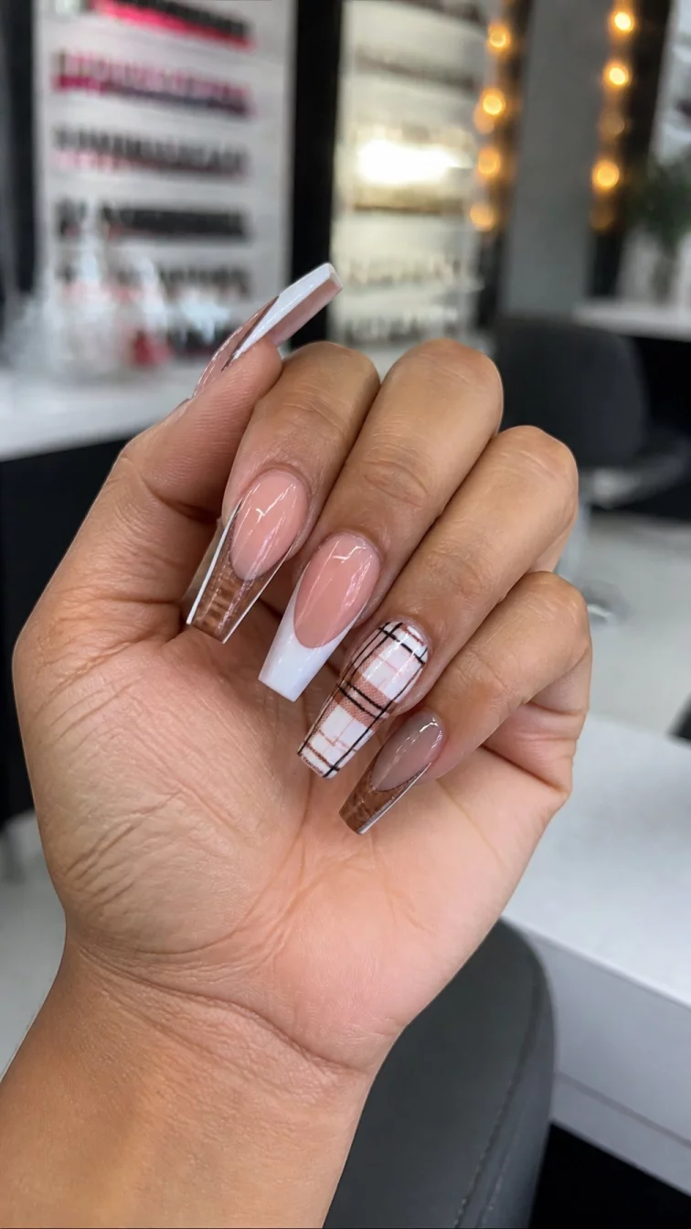 A photorealistic close-up shot of a woman's medium skin tone hand with five fingers, showcasing coffin-shaped long nails featuring French tips and textured brown designs, including plaid patterns, nail salon background