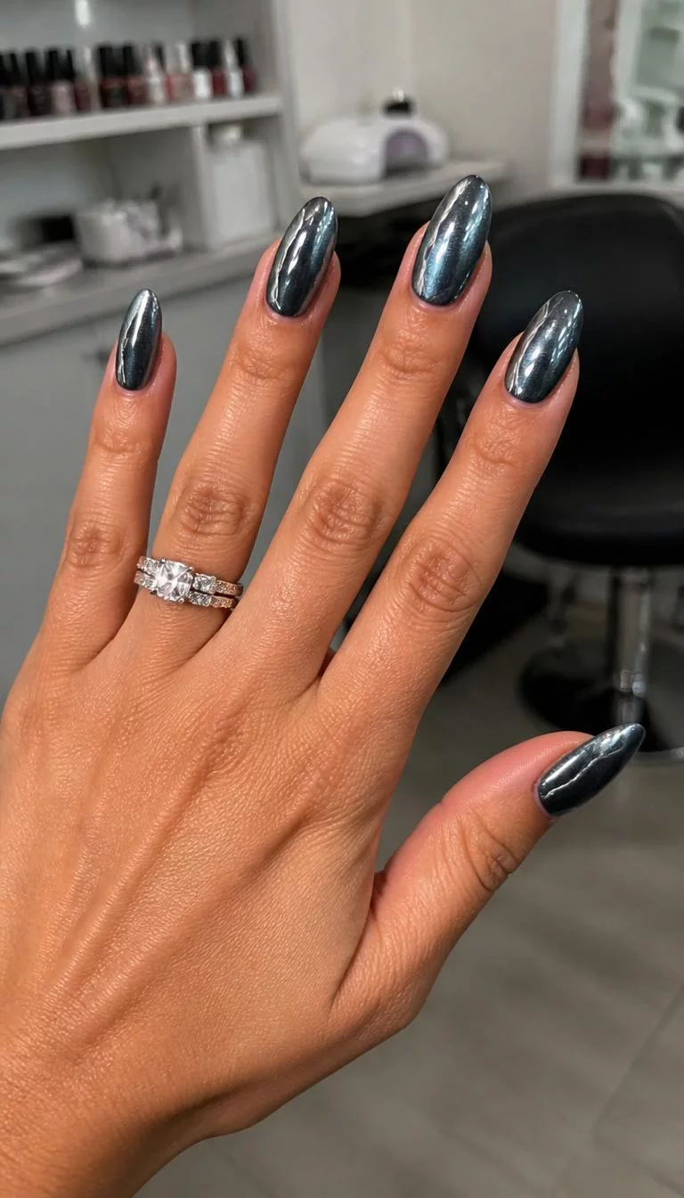 Gunmetal Grey Metallic A photorealistic close-up shot of a woman's tan skin tone hand with five fingers, showcasing almond-shaped long nails featuring a dark, lustrous metallic gunmetal grey color with silver accents, nail salon background