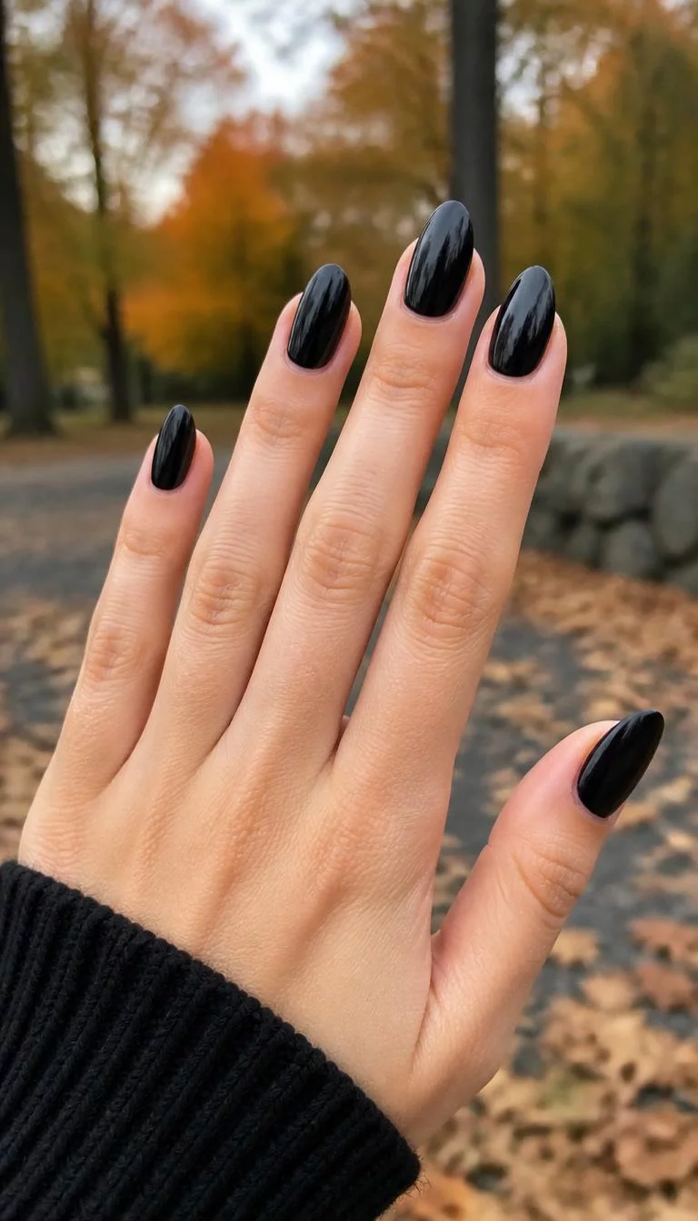 Classic Glossy Almond A photorealistic close-up shot of a woman's light skin tone hand with five fingers, showcasing almond-shaped medium-length nails featuring glossy black paint, outdoor fall background