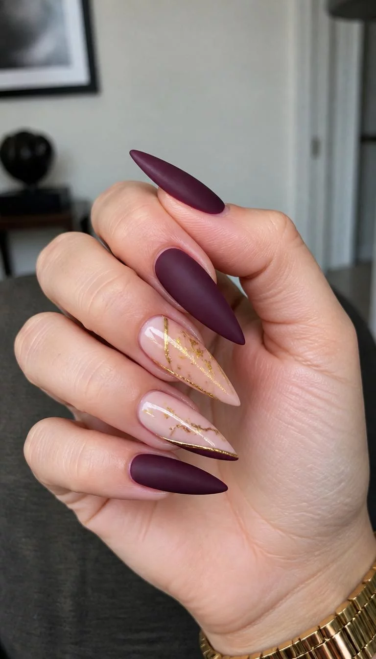 A photorealistic close-up shot of a woman's light skin tone hand with five fingers, showcasing stiletto-shaped long nails featuring a matte deep plum color and light pink accents with gold leaf details, indoor background
