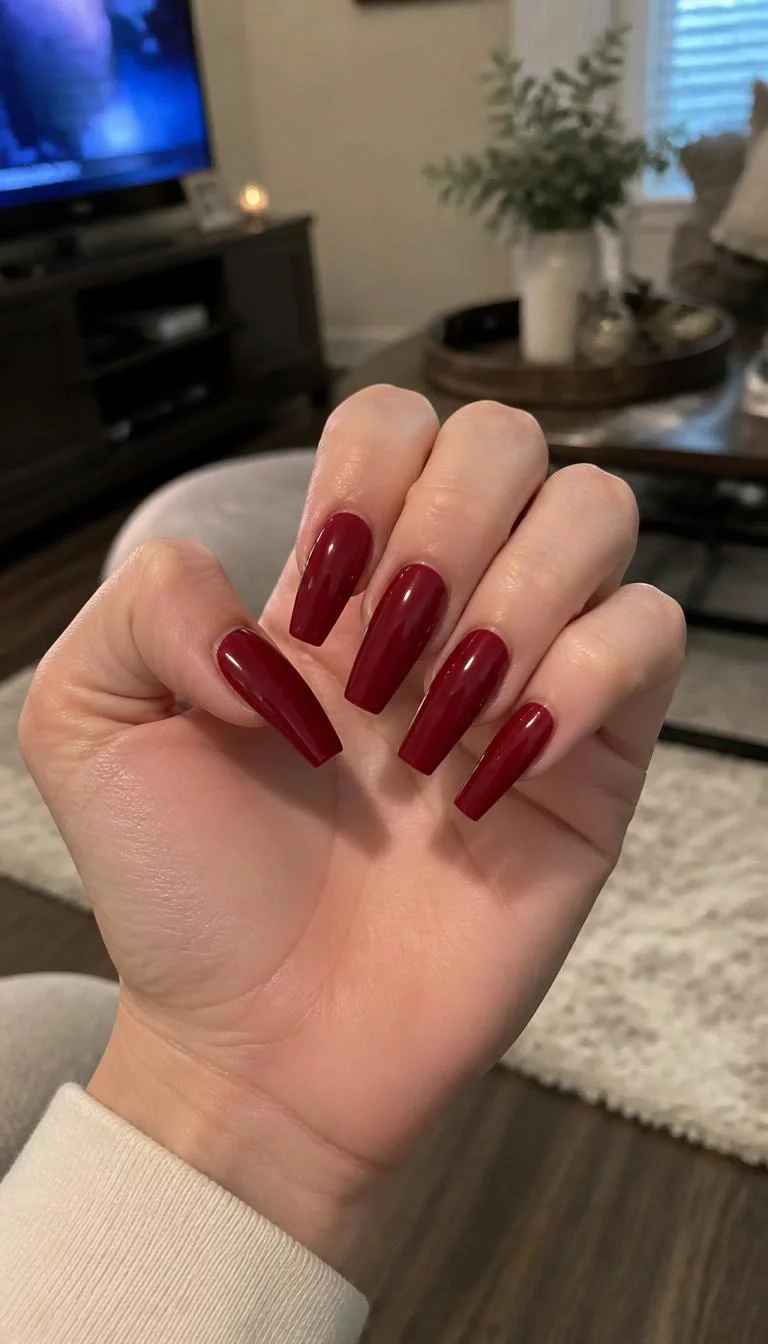 A photorealistic close-up shot of a woman's fair skin tone hand with five fingers, showcasing long coffin-shaped nails featuring a solid deep red polish, living room background