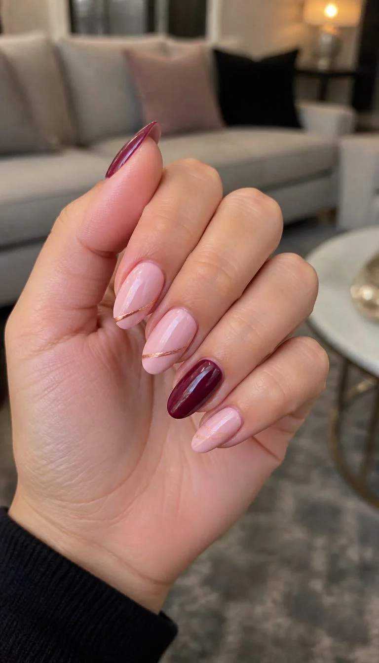 Deep Maroon And Rose Gold Elegance A photorealistic close-up shot of a woman's medium skin tone hand with five fingers, showcasing almond-shaped medium-length nails featuring a light pink base, deep maroon accent nails, and delicate rose gold stripes, living room background