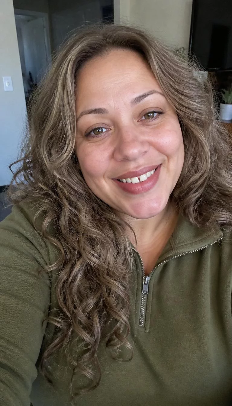 Toasted Walnut Brunette selfie of a 43-year-old Mixed-race woman with a oblong face, fair, straight nose, straight eyebrows, and heart-shaped lips. Her face features gap between front teeth, faint under-eye shadows, and subtle natural facial asymmetry. She has hooded brown eyes, rounded cheeks, broad smile, playful. She is plus-size and is wearing a Olive Green Quarter-Zip Pullover with light ashy brown long voluminous curls hair, overcast daylight, indoor