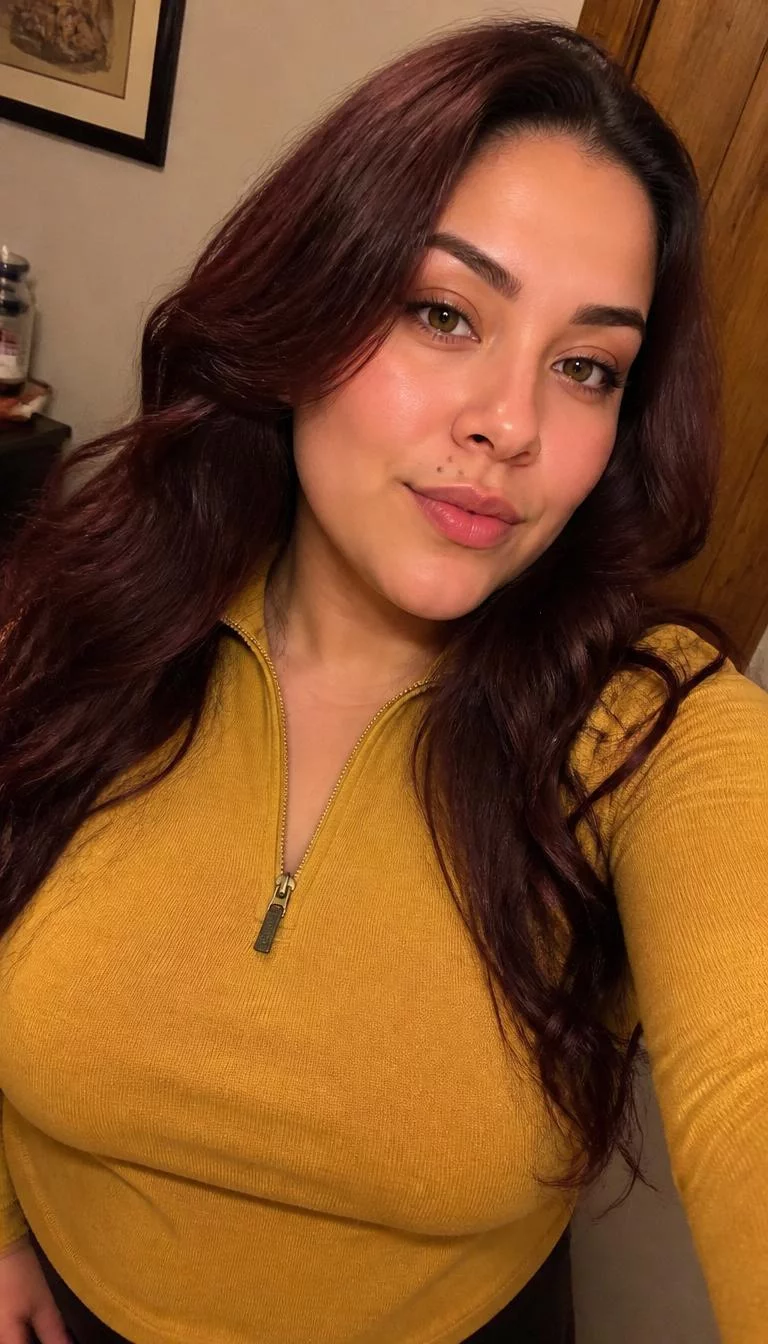 selfie of a 32-year-old Latina woman with a oblong face, light, narrow nose, thick natural eyebrows, and wide lips. Her face features beauty mark near the lip, slightly flushed cheeks, and subtle natural facial asymmetry. She has deep-set amber eyes, soft cheekbones, subtle smile, confident. She is curvy and is wearing a Mustard Yellow Quarter-Zip Pullover with rich mahogany wood long wavy hair, warm indoor lighting, indoor
