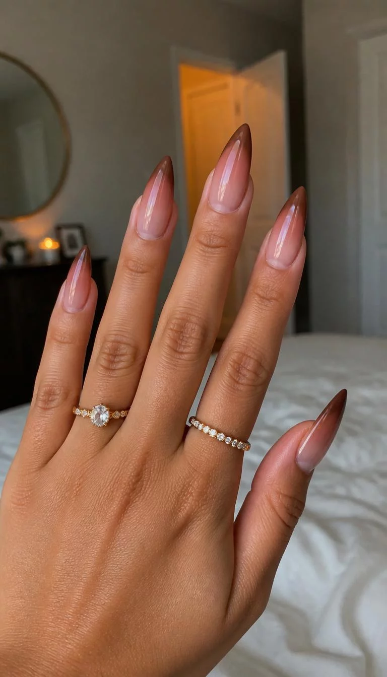 Rich Espresso Stiletto A photorealistic close-up shot of a woman's tan skin tone hand with five fingers, showcasing long stiletto-shaped nails with a rich brown to sheer ombre gradient, bedroom background