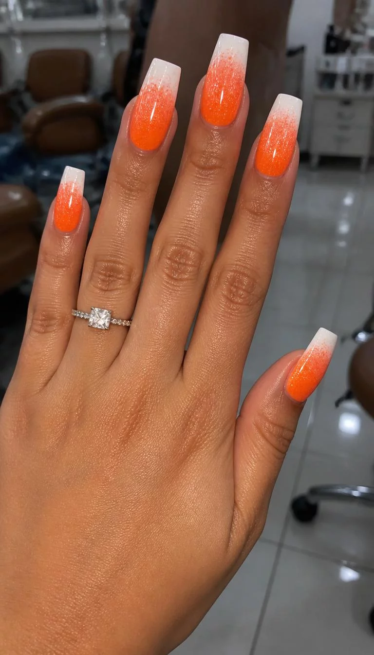 Bright Orange Glitter Burst A photorealistic close-up shot of a woman's olive skin tone hand with five fingers, showcasing square-shaped long nails with a bright orange to white ombre glitter design, nail salon background