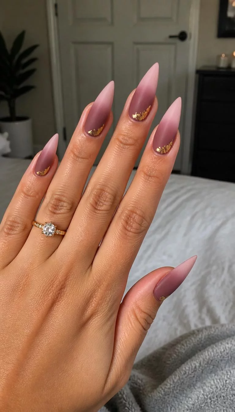 Mauve And Gold Foil A photorealistic close-up shot of a woman's medium skin tone hand with five fingers, showcasing long pointed nails with a matte mauve gradient fading into a pale pink, with a gold foil accent, bedroom background
