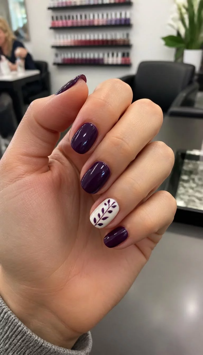 Vine Designs on Deep Purple A photorealistic close-up shot of a woman's light skin tone hand with five fingers, showcasing oval short nails featuring deep purple polish and one white accent nail with a vine design, nail salon background
