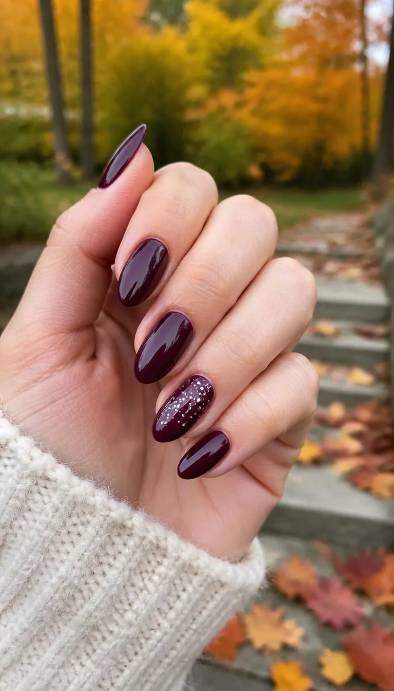 Deep Berry With Speckled Detail A photorealistic close-up shot of a woman's light skin tone hand with five fingers, showcasing almond medium-length nails featuring deep berry polish and one nail with white specks, outdoor fall background